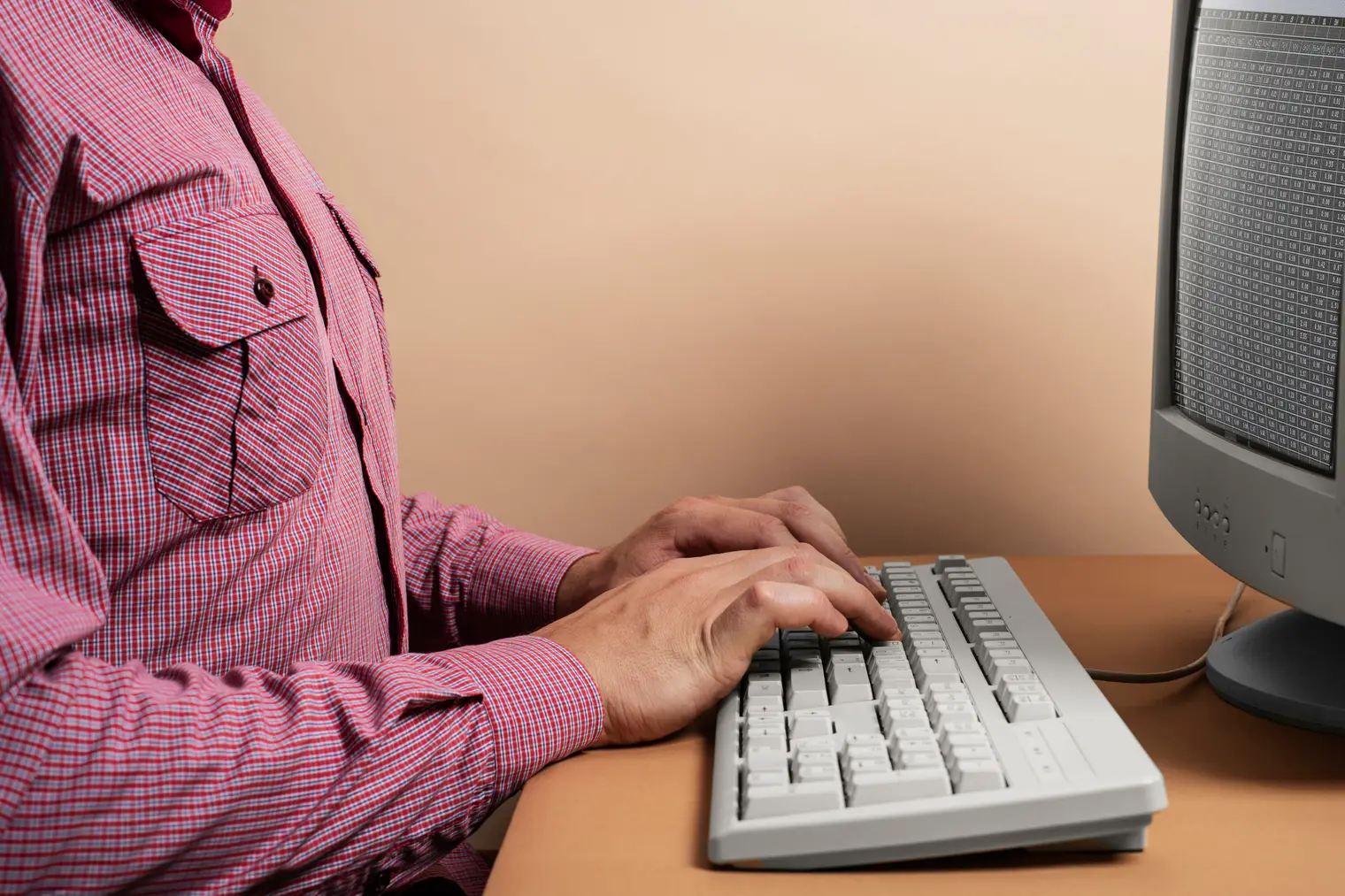 Person taster på et beige tastatur foran en billedrørsskærm som på en computer fra 1990'erne