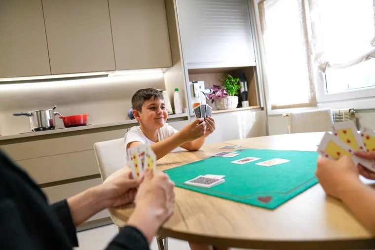 En dreng spiller kort med sine forældre ved køkkenbordet og smiler over sine kort